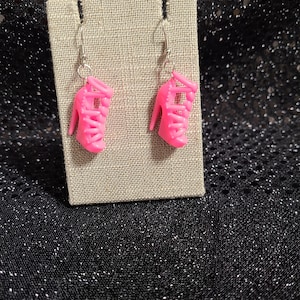 May include: A pair of pink high heel shoe earrings. The earrings are made of plastic and have a silver hook.