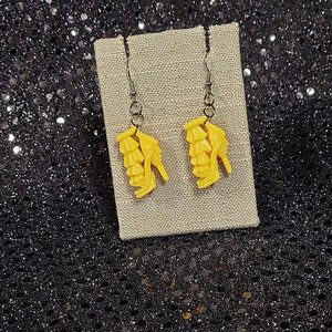 May include: A pair of yellow high heel shoe earrings hanging on a beige card.