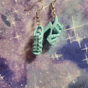 May include: A pair of light blue shoe-shaped earrings with silver hooks. The shoes have a textured design and are made of plastic.