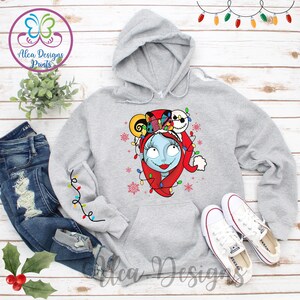 Op de afbeelding: Een grijze hoodie met een kerstthema-afbeelding met een personage uit de film The Nightmare Before Christmas. Het personage draagt ​​een kerstmanmuts en heeft kerstverlichting om zijn hoofd. De afbeelding bevindt zich in het midden van de hoodie.