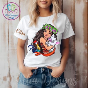 May include: White t-shirt featuring a cartoon image of a girl with long brown hair wearing a flower crown and holding a pig and a rooster. The text "Elisa" is printed on the shirt.