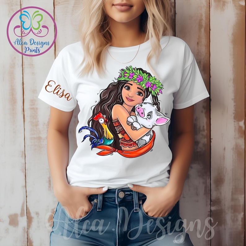 May include: White t-shirt featuring a cartoon image of a girl with long brown hair wearing a flower crown and holding a pig and a rooster. The text "Elisa" is printed on the shirt.
