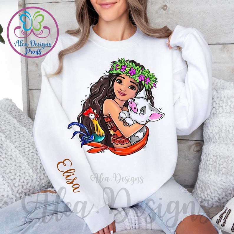 May include: White sweatshirt featuring a colourful cartoon image of a girl with a flower crown, a pig, and a rooster. The text "Elisa" is on the sleeve of the sweatshirt.