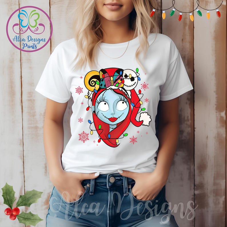 Op de afbeelding: Wit T-shirt met een kleurrijke kerstthema-afbeelding van Sally uit The Nightmare Before Christmas. De afbeelding toont Sally met een kerstmanmuts en Jack Skellington's hoofd op haar hoofd.