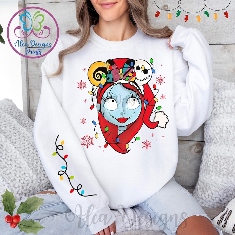 Op de afbeelding: Witte trui met een kleurrijke afbeelding van een personage uit The Nightmare Before Christmas dat een kerstmanmuts draagt en omringd is door kerstverlichting. Het personage heeft blauwe huid, zwart haar en rode lippen.