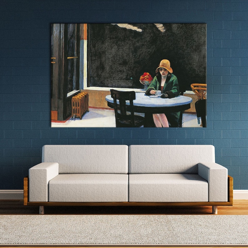 K&ouml;nnte beinhalten: Ein gro&szlig;er gerahmter Druck von Edward Hoppers Gem&auml;lde "Nighthawks". Das Kunstwerk zeigt eine Frau mit Hut, die an einem Tisch in einem Diner sitzt. Das Diner hat ein gro&szlig;es Fenster und einen dunklen Hintergrund. Der Druck wird &uuml;ber einem wei&szlig;en Sofa an einer blauen Backsteinmauer ausgestellt.