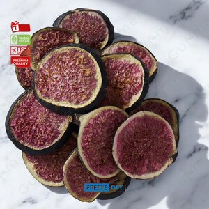 May include: A pile of dried fig slices, freeze-dried and arranged on a white marble surface. The figs are a deep purple colour with a dark brown outer skin. The text "FREEZE-DRY" is visible at the bottom of the image.