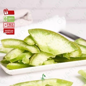 May include: A white ceramic dish filled with green candied citrus peel. The peel is arranged in a pile, with some pieces overlapping.