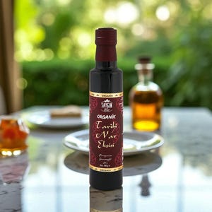 Peut inclure: Une bouteille en verre foncé avec un bouchon et une étiquette bordeaux, remplie d'un liquide foncé. L'étiquette indique "ORGANIK Tarihi Nar Ekşisi". La bouteille est sur une surface réfléchissante.