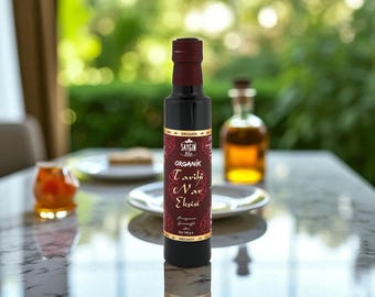 May include: A dark glass bottle with a burgundy cap and label, filled with a dark liquid. The label reads "ORGANIK Tarihi Nar Ekşisi" in a decorative font. The bottle is on a reflective surface.