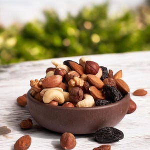 May include: A brown bowl filled with a variety of nuts and dried fruit, including almonds, cashews, hazelnuts, walnuts, and raisins. The bowl is sitting on a white wooden surface.