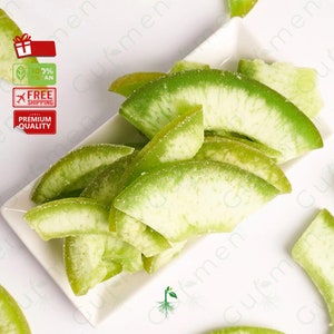 May include: A white ceramic dish filled with green candied citrus fruit slices. The fruit is arranged in a decorative pattern and has a light green color.