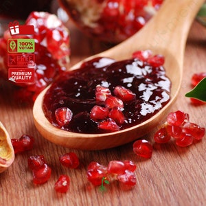 May include: A wooden spoon filled with red pomegranate jam and surrounded by pomegranate seeds on a wooden surface. The spoon is made of light brown wood and has a natural finish. The jam is a deep red colour and has a glossy finish. The seeds are a bright red colour and are scattered around the spoon.