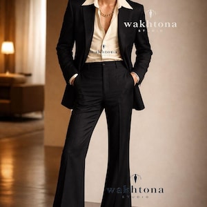 Op de afbeelding: Een zwart pak met een crèmekleurig overhemd en een gouden ketting. De colbertjas wordt gecombineerd met een uitlopende broek. De afbeelding bevat de tekst "wakhtona STUDIO".