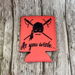 May include: Red can cooler with a black and white illustration of a pirate with crossed swords and the text "As you wish..."