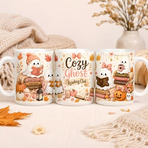 Puede incluir: Tres tazas de cer&aacute;mica blanca con ilustraciones de fantasmas leyendo libros, calabazas y hojas de oto&ntilde;o. La taza central muestra el texto 'Cozy Ghost Reading Club' en letras marrones y rosas, rodeado de peque&ntilde;as estrellas, un lazo y una vela.
