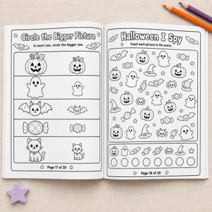 May include: An open activity book with black and white line art pages. The left page features a Circle the Bigger Picture exercise with Halloween icons. The right page shows a Halloween I Spy game with counting tasks. Two colored pencils and a star shape are visible.