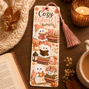Puede incluir: Un marcap&aacute;ginas rectangular con el texto Cozy Ghost Reading Club, decorado con ilustraciones de tres fantasmas blancos leyendo libros, pilas de libros, calabazas, tazas y hojas de oto&ntilde;o, rematado con una borla rosa en la parte superior.