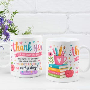 Op de afbeelding: Twee witte keramische mokken met kleurrijke afbeeldingen. Eén mok toont de tekst 'thank you FOR ALL THAT YOU DO! YOU INSPIRE, YOU ENCOURAGE, YOU BELIEVE, YOU CARE... YOU MAKE A DIFFERENCE every day!' en 'Mrs Seavey'. De andere toont een roze mok met pennen op een stapel boeken en een rode appel.