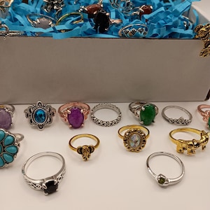 Puede incluir: Una colección de anillos de plata, oro y oro rosa con varias piedras y diseños. Los anillos presentan piedras turquesa, verdes, moradas y negras. Algunos anillos tienen diseños intrincados, mientras que otros son bandas simples.