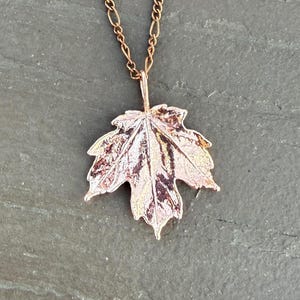 May include: A rose gold maple leaf pendant necklace. The pendant is a detailed replica of a maple leaf, suspended from a delicate chain. The necklace is a nature-inspired piece of jewelry.