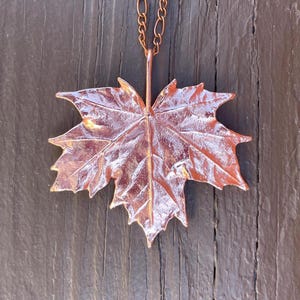 May include: A copper maple leaf pendant necklace with a delicate chain. The leaf is detailed with veins and a textured surface.