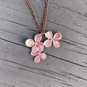 May include: A delicate copper necklace with a pendant featuring a cluster of five pink flower charms.