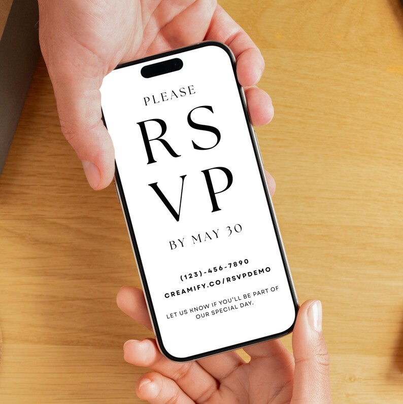 May include: A smartphone displaying a digital RSVP invitation. The screen features the words "PLEASE RSVP BY MAY 30" in a bold, elegant font. Contact information and a website address are also visible. The phone is held against a light wooden surface.