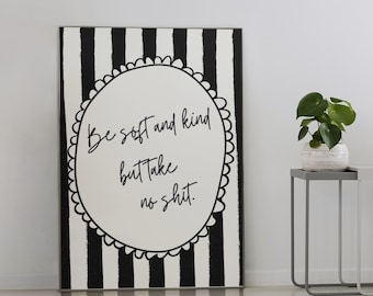 May include: A black and white striped canvas with the text "Be soft and kind but take no shit." A small potted plant, books, and a lamp sit on two side tables. A striped rug is on the floor.