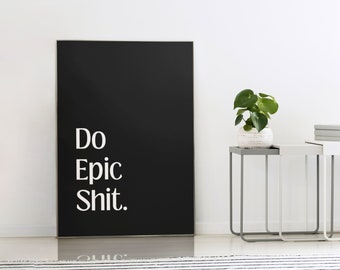 Puede incluir: Arte mural enmarcado en negro con el texto blanco «Do Epic Shit». La obra de arte está apoyada contra una pared blanca. Una pequeña planta en una maceta blanca se encuentra sobre una mesa auxiliar gris y blanca.