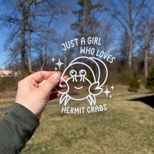 May include: White vinyl sticker with a cartoon hermit crab and the text "Just a girl who loves hermit crabs".