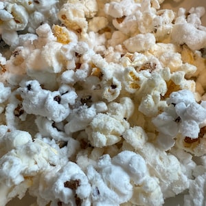 Puede incluir: Primer plano de un montón de palomitas de maíz. Las palomitas son en su mayoría blancas con algunos granos amarillos y marrones visibles. Las palomitas parecen recién hechas y ligeramente saladas.