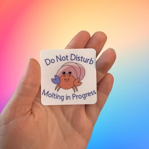 May include: A white sticker with a cartoon hermit crab molting. The sticker says "Do Not Disturb Molting in Progress".