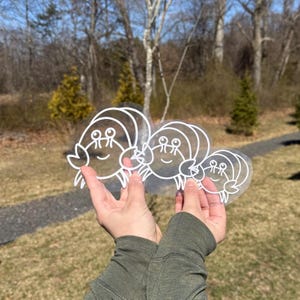 May include: Three white vinyl stickers of a cartoon crab with a smiling face. The stickers are layered on top of each other, with the largest sticker in the back and the smallest sticker in the front.