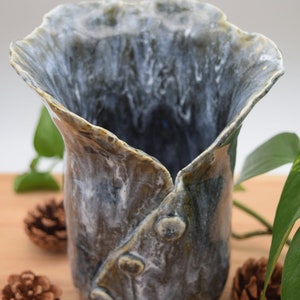 May include: A handcrafted ceramic vase with a unique, organic shape. The vase features a blend of blue, green, and brown hues, with a textured surface and decorative elements. The vase is approximately 7 inches tall.