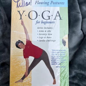 Peut inclure: Une vidéo d'instruction de yoga intitulée "Lilias! Flowing Postures YOGA pour débutants". La couverture présente une femme démontrant une posture de yoga. La série comprend Arms & Abs, Serenity Now, Legs & Buns et Cardio Challenge. La série complète de yoga est visible.