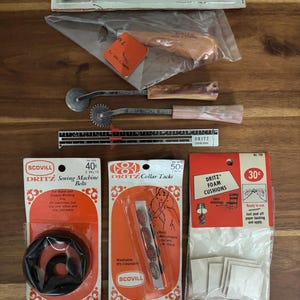 May include: A collection of vintage sewing notions including a Dritz dressmaker marking pencil, a wooden handle tool, two tracing wheels with patterned handles, a 6-inch Dritz sewing gauge, sewing machine belts, collar tacks, and foam cushions.