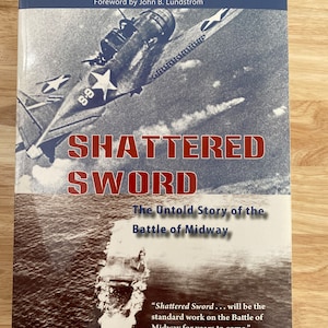 May include: A book cover with a black and white photo of a plane flying over the ocean. The book title is "Shattered Sword: The Untold Story of the Battle of Midway".