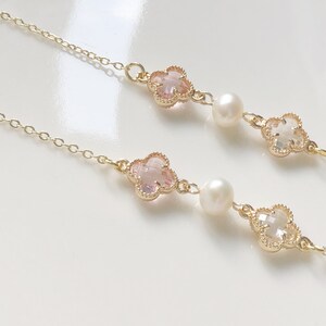 May include: A delicate gold chain necklace with two pink and white clover charms and pearl accents.