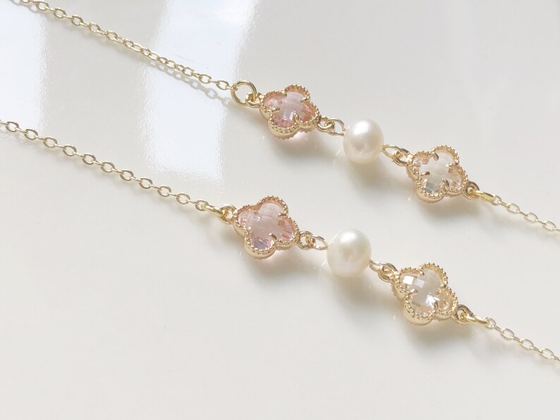 May include: A delicate gold chain necklace with two pink and white clover charms and pearl accents.