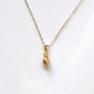 Op de afbeelding: Een gouden ketting met een klein ananas-hanger.