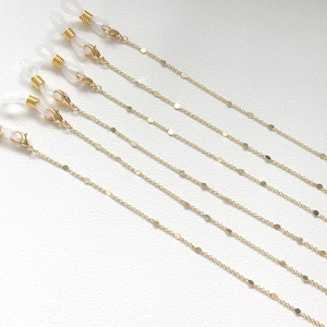 May include: Set of six gold-tone eyeglass chains with small, round, flat links. Each chain has clear plastic loops at the ends.