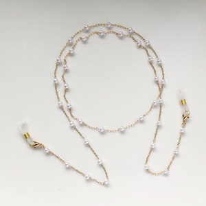 May include: A gold chain with white pearl beads and clear plastic clasps. The chain is doubled and can be used as a glasses chain.