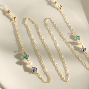 May include: Gold chain with blue and green clover charms and white pearls. The chain has two loops at the ends for attaching to glasses.