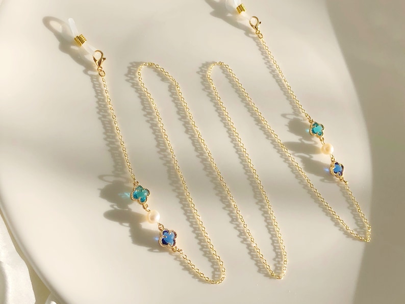 May include: Gold chain with blue and green clover charms and white pearls. The chain has two loops at the ends for attaching to glasses.