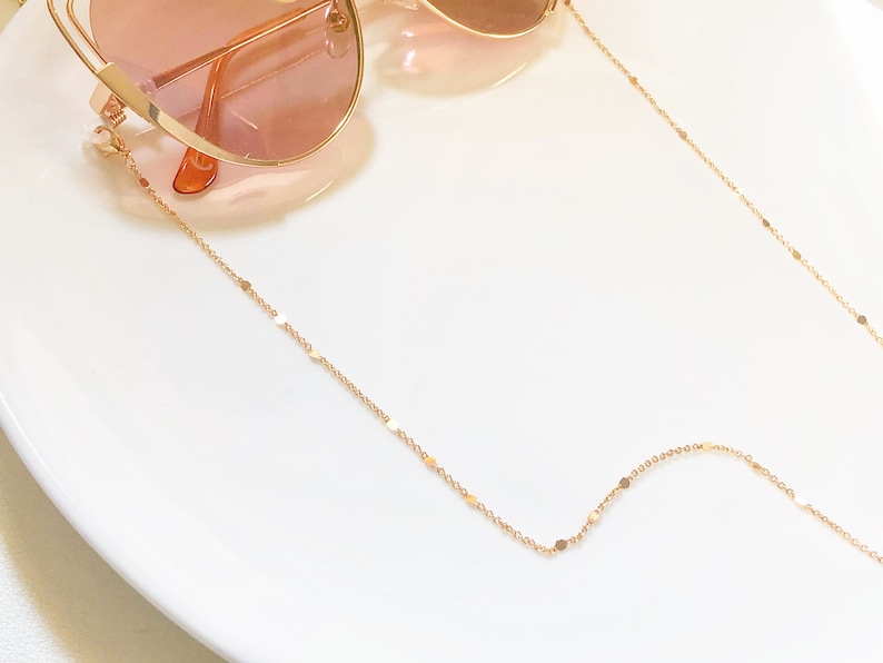 Op de afbeelding: Een gouden ketting met kleine, platte, ronde schakels. De ketting is ontworpen om brillen vast te houden.