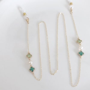 May include: A gold chain with green clover charms and white pearls. The chain has two clasps for attaching to glasses.