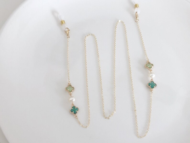May include: A gold chain with green clover charms and white pearls. The chain has two clasps for attaching to glasses.