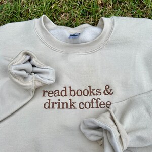 May include: A beige sweatshirt with the text "read books & drink coffee" embroidered in brown on the front.