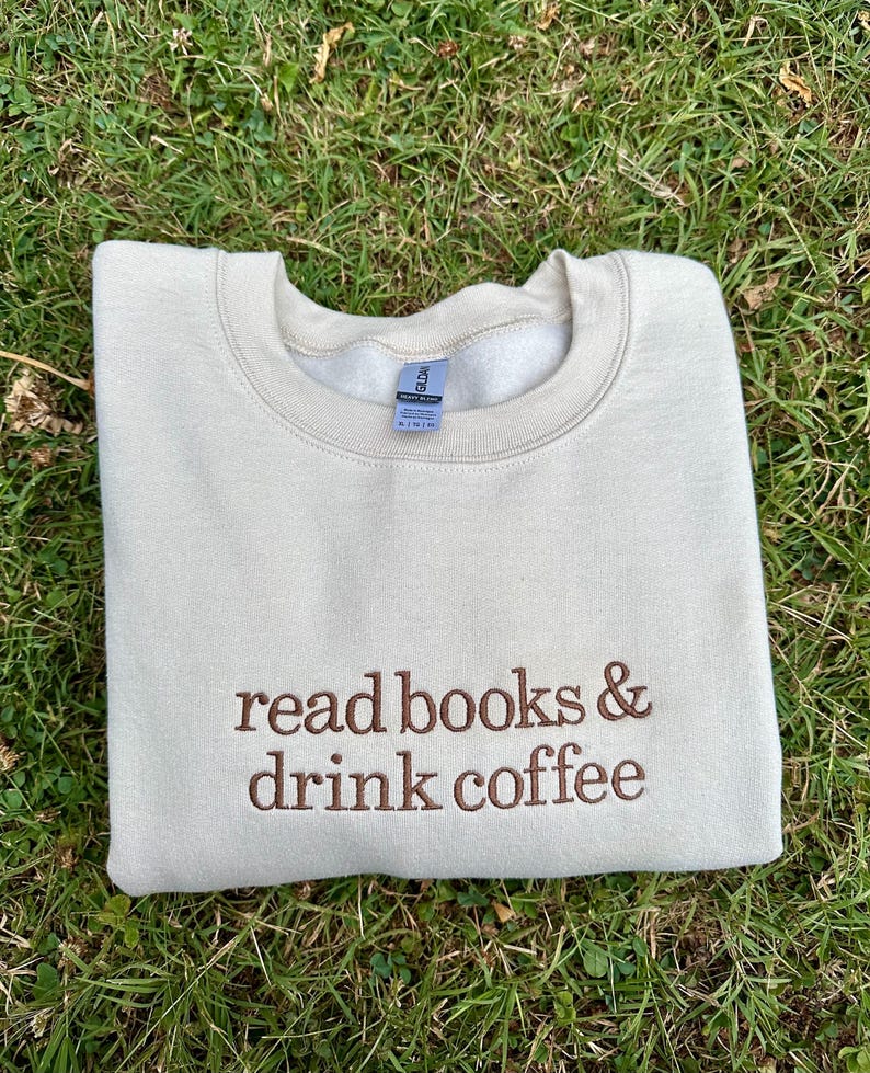 May include: A beige sweatshirt with the text "read books & drink coffee" embroidered in brown on the front.